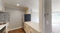 This single-floor residence offers a thoughtfully designed layout with a blend of modern updates and comfortable living spaces. The galley-style kitchen is a standout feature, showcasing white shaker cabinetry crowned with elegant molding, quartz countertops, a mosaic tile backsplash in grey and white tones, and a full suite of stainless steel appliances including a refrigerator, range, dishwasher, and over-the-range microwave. Warm hardwood-style flooring runs throughout the kitchen and connects seamlessly to adjacent areas. The bedrooms are generously sized, bathed in natural light through wide windows that offer views of surrounding greenery. Each room features soft wall-to-wall carpeting, crown molding, and ceiling fans with integrated lighting, contributing to a comfortable and airy atmosphere. The bathrooms are well-appointed with white vanity cabinetry, quartz countertops, brushed gold fixtures, a mosaic tile backsplash above the vanity, and a tub-shower combination enclosed by sliding glass doors. Dark hardwood-style flooring in the bathrooms adds a refined contrast to the light finishes. Crown molding is consistent throughout the unit, lending a cohesive and polished character to the entire space.