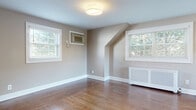 Located at 14 Bliss Ave in Tenafly, NJ, this single-floor residence offers a thoughtfully designed layout with a warm, neutral color palette throughout. Rich hardwood floors flow seamlessly across the living and bedroom areas, complementing the soft taupe wall tones and crisp white trim and baseboards.

The kitchen is a functional highlight, outfitted with white shaker-style cabinetry, dark countertops, and a full suite of stainless steel appliances including a gas range, over-the-range microwave, dishwasher, and refrigerator. Tile flooring in the kitchen area provides a clean transition between spaces.

The bedrooms feature the same warm hardwood floors and are filled with natural light from multiple windows dressed with white blinds. Angled architectural ceiling details in one room add character, while wall-mounted air conditioning units and decorative radiator covers provide year-round climate comfort.

The bathroom is finished with bright marble-style wall tile, a decorative mosaic accent border, a soaking tub, and a white vanity with storage — conveying a clean, polished aesthetic.

Throughout the home, generous windows frame views of surrounding greenery, lending each room a serene, connected-to-nature ambiance that enhances the overall sense of comfort and livability.