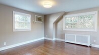 Located at 14 Bliss Ave in Tenafly, NJ, this single-floor residence offers a thoughtfully designed layout with a warm, neutral color palette throughout. Rich hardwood floors flow seamlessly across the living and bedroom areas, complementing the soft taupe wall tones and crisp white trim and baseboards.

The kitchen is a functional highlight, outfitted with white shaker-style cabinetry, dark countertops, and a full suite of stainless steel appliances including a gas range, over-the-range microwave, dishwasher, and refrigerator. Tile flooring in the kitchen area provides a clean transition between spaces.

The bedrooms feature the same warm hardwood floors and are filled with natural light from multiple windows dressed with white blinds. Angled architectural ceiling details in one room add character, while wall-mounted air conditioning units and decorative radiator covers provide year-round climate comfort.

The bathroom is finished with bright marble-style wall tile, a decorative mosaic accent border, a soaking tub, and a white vanity with storage — conveying a clean, polished aesthetic.

Throughout the home, generous windows frame views of surrounding greenery, lending each room a serene, connected-to-nature ambiance that enhances the overall sense of comfort and livability.