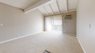 Located in Brea, CA, this 2-bedroom, 2-bathroom residence offers a well-organized single-level layout designed for comfortable everyday living. The living room is an immediate standout, featuring striking vaulted ceilings with exposed white wood beams that lend architectural character and a sense of openness. Sliding glass doors lead out to a private balcony, filling the space with natural light. The galley-style kitchen is thoughtfully designed with white cabinetry, dark granite countertops, black appliances, a built-in dishwasher, and wood-look flooring — with a pass-through window connecting it to the adjacent dining area. A pantry provides additional storage convenience. The spacious primary bedroom features plush carpeting, a mirrored sliding-door closet, and windows that invite natural light. The second bedroom also offers comfortable proportions with carpet flooring and ample wall space. Both bathrooms are finished with white cabinetry, dark granite countertops, and tub-shower combinations. Throughout the home, a warm neutral color palette, white trim, and textured ceilings create a cohesive and inviting ambiance. Three closets across the unit ensure generous storage throughout.