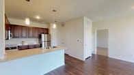 This single-floor residence offers a thoughtfully designed open-concept layout that seamlessly connects the kitchen and living areas. The kitchen is a standout feature, equipped with rich dark wood cabinetry, granite-look countertops, a full suite of stainless steel appliances including a refrigerator, range, and over-the-range microwave, and a peninsula with a built-in sink. Pendant lighting above the peninsula adds a refined touch, while durable hardwood-style flooring extends throughout the main living and kitchen spaces.

The living area is bright and welcoming, with multiple windows dressed in horizontal blinds that invite natural light while maintaining privacy. A door provides direct access to the outdoors from the living space. The bedrooms feature plush wall-to-wall carpeting and windows that allow for comfortable natural light. The primary bedroom includes a ceiling fan for added comfort.

The full bathroom is finished with dark wood cabinetry, granite-look countertops, a large vanity mirror, hardwood-style flooring, and a tiled shower-tub combination. Clean white tile work and brushed nickel fixtures complete the polished look. An attached garage with a sectional door provides secure, convenient parking and additional storage space.