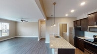 Located at 18300 Wheeler Rd in Westfield, Indiana, this single-floor residence offers a thoughtfully designed open-concept layout that seamlessly connects the kitchen, dining, and living areas. The kitchen is a standout feature, showcasing rich dark-stained cabinetry, light granite countertops, a subway tile backsplash, stainless steel appliances including a refrigerator, range, and built-in microwave, and a kitchen island with pendant lighting and an undermount sink. Hardwood-style flooring flows throughout the main living areas, complementing the neutral warm-toned walls and crisp white trim. The spacious living room is finished with crown molding, a ceiling fan, and sliding glass doors that invite natural light and provide outdoor access. Bedrooms feature plush carpeting and generous windows that bring in ample natural light. The bathroom is well-appointed with a granite-topped vanity, dark cabinetry, a framed mirror, and a shower-tub combination. A dedicated laundry area with side-by-side washer and dryer connections adds everyday convenience. The overall ambiance is clean, modern, and move-in ready, offering a comfortable and functional living environment.