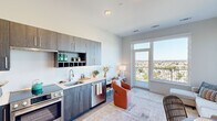 This thoughtfully designed single-floor unit offers a seamless open-concept layout that integrates the kitchen, dining, and living areas into one cohesive space. The kitchen is outfitted with dark wood-grain cabinetry reaching toward the ceiling, a built-in wine rack, light quartz countertops, and a full suite of stainless steel appliances including a French door refrigerator, electric range, and dishwasher. Light wood-style flooring runs throughout the kitchen, grounding the contemporary aesthetic.

The living and dining area is generously proportioned and bathed in natural light from expansive floor-to-ceiling windows that frame sweeping elevated views of the surrounding cityscape and greenery. A glass door leads to a private balcony, extending the living space outdoors and enhancing the sense of openness.

The bedroom area is set apart from the main living space, offering privacy, with ample closet storage visible along one wall. The bathroom is finished to a high standard, featuring large-format white marble-style floor and wall tiles, a frameless glass walk-in shower, a floating wood-tone vanity with a white countertop, and a well-lit mirror — creating a clean, spa-like atmosphere. Overall, the unit presents a refined, modern living environment with high-quality finishes throughout.