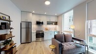 This single-floor unit presents a thoughtfully designed open-concept layout where the kitchen and living area flow seamlessly together. The kitchen is outfitted with contemporary white cabinetry extending to the ceiling, providing generous storage, and is equipped with stainless steel appliances including a refrigerator, gas range, and built-in microwave. A single-basin sink sits beneath a large window that draws in abundant natural light, brightening the entire main living space. Light hardwood flooring runs throughout, reinforcing the unit's clean, modern aesthetic.

The living area comfortably accommodates seating and benefits from a large window offering views of the surrounding building exterior, further enhancing the sense of openness. The bedroom is a well-proportioned retreat featuring a bold geometric wall mural as a focal point, a reach-in closet with rod and shelving, and a large window that admits ample natural light. Light hardwood flooring continues here, maintaining consistency across the unit.

The bathroom is finished with tile-surround tub and shower combination, wood-look flooring, a white vanity with integrated sink, a lighted mirror, and glass shelving, creating a clean and functional space. Overall, the unit delivers a cohesive, contemporary aesthetic with practical finishes throughout.