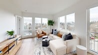 Located at 825 NE 63rd St in Seattle's Ravenna neighborhood, this thoughtfully designed one-bedroom, one-bathroom residence offers a bright and efficient layout with modern finishes throughout. Light wood-tone flooring flows seamlessly from the entry hallway through the living area, creating a warm, cohesive aesthetic against crisp white walls.

The living room is a standout space, anchored by large corner windows that frame sweeping views of the Seattle skyline and surrounding neighborhood. Natural light fills the room throughout the day, and a sliding glass door opens to a private balcony, extending the living space outdoors. The kitchen sits adjacent to the living area and features light wood cabinetry extending to the ceiling, maximizing storage.

The bedroom offers a peaceful retreat with a tall window framing city views, warm wood flooring, and a generous built-in closet with sleek sliding doors. A dedicated laundry closet with a stacked Whirlpool washer and dryer adds everyday convenience.

The bathroom is finished with a light wood vanity, white quartz countertop, large mirror, and a shower-tub combination. A clean hallway connects all rooms efficiently, completing this well-appointed urban residence.