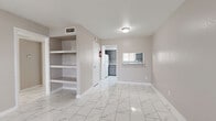 This two-bedroom, three-bathroom single-floor home at 6203 Marinette Dr in Houston, Texas offers a well-organized layout with consistent, modern finishes throughout. The living area is anchored by striking marble-look porcelain tile flooring that runs continuously through the space, lending a clean and polished aesthetic. Built-in open shelving is integrated into the living area wall, providing practical display and storage solutions. A pass-through window connects the living room to the kitchen, promoting an open feel between the two spaces. The kitchen features gray cabinetry, granite-style countertops, a decorative patterned tile backsplash, and ample counter and storage space. Both bedrooms are generously proportioned, with the primary bedroom offering a notably spacious footprint. Natural light enters through windows fitted with blinds. A dedicated walk-in closet with built-in shelving and hanging rods serves the primary bedroom. The three bathrooms are finished with the same marble-look tile flooring and include vanities topped with granite-style countertops and large mirrors. Neutral warm-gray walls tie the interior together, creating a cohesive and move-in-ready atmosphere throughout the home.
