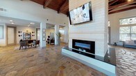 This single-story amenity facility offers a well-rounded collection of spaces designed for both recreation and productivity. The welcoming lounge area features rich slate tile flooring, a tufted leather bench beneath soaring windows that flood the space with natural light, and curated wall décor including framed certificates. Adjacent to the lounge is a cozy seating area with a brown sofa, cowhide rug, and warm recessed lighting, accented by clerestory windows that add to the open, airy atmosphere.

The fitness center is comprehensively equipped, featuring a dedicated weight room with a cable machine, squat rack, and free weights, alongside a cardio area with treadmills, a stationary bike, and a weight bench. An inspirational fitness-themed mural energizes the space, which also benefits from natural light through multiple windows and glass double doors leading outdoors. A separate area provides stability balls and additional accessories.

A game room with hardwood-style flooring offers a wall-mounted TV and oversized Connect Four for leisure. The business center includes a long floating desk with multiple desktop computers, a printer, and industrial-style stools. The kitchenette stands out with striking cedar plank wood walls, dark granite countertops, white cabinetry, and a built-in stainless steel appliance suite. A casual dining nook with a high-top table and rustic pallet wall art completes the space.