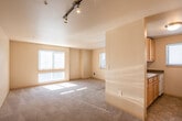 This single-floor residence is thoughtfully laid out to maximize both functionality and comfort. The living area is generously sized, featuring neutral-toned carpet underfoot and warm beige walls that create a bright, welcoming atmosphere. Multiple windows fitted with horizontal blinds allow natural light to flow freely throughout the space, casting sunlight across the open floor plan. Track lighting is installed along the ceiling, providing versatile illumination options. A pass-through counter connects the living area to the kitchen, enhancing the open feel between the two spaces.

The kitchen is efficiently designed with light wood cabinetry offering ample storage, dark laminate countertops, tile flooring, and white appliances including a dishwasher and electric range. A window above the counter brings in additional natural light. The bedroom is a comfortable, carpeted retreat with its own window providing natural light and views of the surrounding area.

The bathroom features tile flooring, a light wood vanity with a stone-toned countertop, and a separate water closet housing a full soaking tub. Throughout the unit, the neutral color palette and practical finishes create a clean, move-in-ready environment suitable for a variety of lifestyles.