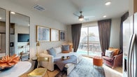 This thoughtfully designed single-floor unit offers a seamless blend of modern style and functional living. The open-concept living area serves as the heart of the space, featuring light hardwood flooring, recessed lighting, and a ceiling fan overhead. A plush sofa anchored by a patterned area rug sits beneath a curated gallery of framed artwork, while large sliding glass doors flood the room with natural light and offer direct views of an outdoor pool. Floor-length charcoal drapes frame the expansive window, adding a refined, contemporary touch.

Adjacent to the living area, a compact dining nook with a round table and gold-accented chairs is complemented by full-length mirrors that enhance the sense of openness. The kitchen is efficiently appointed with taupe cabinetry, white countertops, and stainless steel appliances including a range with over-the-range microwave. A dedicated in-unit laundry closet adds everyday convenience.

The bathroom features light hardwood-style flooring, a vanity with grey cabinetry, and decorative wall-mounted shelving. Throughout the unit, a warm neutral palette accented with burnt orange and gold tones creates a cohesive and inviting ambiance, making this space as visually appealing as it is practical.