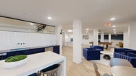 Located at 2900 W Hamlin Rd in Rochester Hills, Michigan, this thoughtfully designed amenity space offers a diverse range of recreational and social zones across a single, generously sized floor. The interior is defined by a cohesive modern aesthetic, featuring light wide-plank hardwood flooring, crisp white walls with glossy brick tile accents, and structural white columns that subtly define each zone without enclosing the open-plan layout.

A standout feature is the dedicated golf simulator room, equipped with an aboutGOLF projection system, dual projectors, and artificial turf hitting mats — ideal for year-round play. Adjacent to the simulator, a putting green with a curved turf layout flows seamlessly into a comfortable lounge area furnished with warm leather seating and contemporary art.

The main social hub features bold navy blue velvet lounge chairs arranged around a wall-mounted flat-screen TV, creating an inviting media and gathering space. A sleek wet bar with navy cabinetry and a pass-through window serves the adjacent dining area, complete with a white high-top table and bar stools.

A separate room houses a designer ping pong table set against glossy white brick tile walls, while floor-to-ceiling glass partitions with black framing open to a bright, airy lounge filled with natural light. Recessed lighting throughout ensures a polished, well-lit environment across all areas.