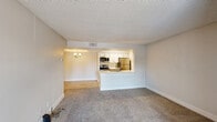 This well-designed one-bedroom, one-bathroom unit offers a functional and comfortable layout across a single floor. The living area is finished with plush carpet and neutral-toned walls, creating a clean, inviting atmosphere. A sliding glass door floods the space with natural light and provides direct access to outdoor views. The textured ceiling and a wall sconce add subtle character to the living area.

The kitchen is positioned at the heart of the unit, accessible via a pass-through counter that opens to the living space. It features stainless steel appliances — including a refrigerator, microwave, and range — along with white cabinetry, a stainless steel sink, and a dishwasher. Light wood-look flooring and light-toned countertops give the kitchen a bright, modern feel.

The bedroom is a well-proportioned private retreat, carpeted for comfort and equipped with a ceiling fan with light fixture. A window with horizontal blinds allows natural light while maintaining privacy.

The bathroom is clean and efficiently laid out, featuring a full tub and shower combination with a curved curtain rod, wood-look tile flooring, and brushed nickel fixtures. The vanity area provides countertop space alongside warm wood cabinetry. Throughout, the unit maintains a consistent neutral palette, offering a move-in ready space with practical finishes.