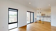 Located at 100 N Farwell St in Eau Claire, Wisconsin, this modern 2-bedroom, 2-bathroom residence offers a thoughtfully designed open-concept layout with clean lines and contemporary finishes throughout. Warm-toned hardwood flooring runs seamlessly through the living areas, complementing the bright white walls and recessed lighting that create an airy, welcoming ambiance. The living room is anchored by large black-framed sliding glass doors and an additional full-glass door, flooding the space with natural light and providing access to a private balcony with outdoor views. The kitchen is well-appointed with white shaker cabinetry, black hardware accents, light quartz countertops, a subway tile backsplash, a natural wood open shelf, stainless steel appliances including a dishwasher and range, and pendant lighting overhead. The entry features a built-in mudroom area with warm wood cabinetry, overhead storage, and coat hooks — a practical and stylish touch. Both bedrooms are generously sized, each with large black-framed windows that bring in natural light and urban views of the surrounding Eau Claire skyline. The bathrooms are finished with clean white surrounds, warm wood vanities, and tile flooring. A dedicated closet rounds out this well-organized and modern living space.