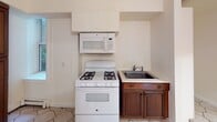 Located on Venice Court in Ridgefield Park, NJ, this basement-level unit offers a practical and well-organized layout across three bedrooms and one bathroom. The space is connected by a long, light-filled hallway finished with classic octagonal ceramic tile flooring and built-in white cabinetry, providing ample storage from the moment you enter.

The bedrooms feature warm hardwood floors and are served by baseboard heating. Several rooms include built-in closets with hanging rods, and windows positioned along the upper portion of the walls bring in natural light throughout. One bedroom is equipped with a ceiling fan and light fixture, while another features track lighting and a large wall mirror that adds a sense of openness.

The kitchen is efficiently designed with dark wood cabinetry, a gas range, over-the-range microwave, and a single basin sink. Hexagonal tile flooring and a window with a deep sill complete the kitchen area, which also includes a tall pantry-style cabinet for additional storage.

The bathroom presents a clean, classic aesthetic with white subway tile surrounding the tub and shower, penny tile flooring, a white vanity, and a window that introduces natural light into the space.