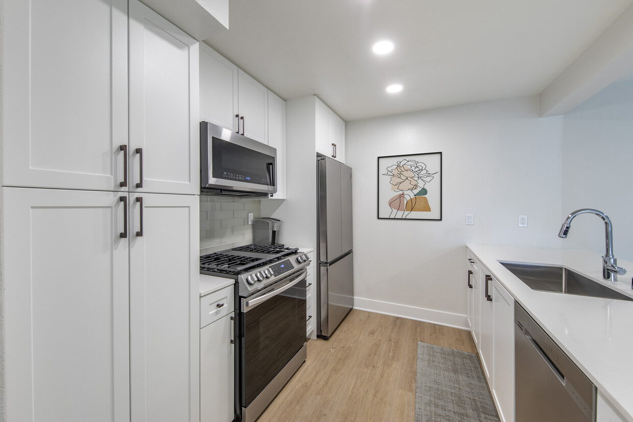 Renovated Package I kitchen with stainless steel appliances, white quartz countertops, white cabinetry, light grey tile backsplash, and hard surface flooring - Avalon Woodland Hills