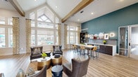 Located at 255 Williamsburg Pkwy in Fate, TX, this single-floor community clubhouse is a thoughtfully designed gathering space that blends modern aesthetics with comfortable functionality. The entry lobby immediately impresses with soaring vaulted ceilings, a dramatic circular chandelier, rich herringbone-patterned flooring, and floor-to-ceiling French doors that flood the space with natural light. A stylish reception desk and plush velvet seating in warm terracotta tones create a welcoming first impression.

The main lounge area is anchored by a stunning floor-to-ceiling marble-style feature wall with an inset flat-screen display, complemented by rich leather furnishings and a wood-paneled accent wall with its own media niche. Exposed wooden beams and a wall of oversized windows frame panoramic views of the outdoor pool area, bringing the outdoors in.

A wet bar and high-top seating area with teal accent walls and modern pendant lighting provide a social hub ideal for casual gatherings. The game room extends the entertainment options with a billiards table, shuffleboard, and curated artwork. A dedicated cyber lounge offers a vibrant, colorful retreat with bench seating and a workstation. Throughout, light wood-look flooring, bold accent walls, and curated art create a cohesive, upscale ambiance.