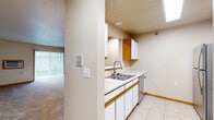 Located at 5001 44th Ave S in Fargo, North Dakota, this one-bedroom, one-bathroom unit offers a practical and well-organized single-floor layout. The kitchen features white cabinetry with warm wood-tone trim, a double-basin stainless steel sink, a dishwasher, and a full-size refrigerator, all set on light tile flooring. Upper and lower cabinet storage provides ample space, and the kitchen opens toward the living area via a half-wall partition. The living room is carpeted and filled with natural light through a sliding glass door fitted with vertical blinds, which leads to an outdoor area. A baseboard heating system and wall-mounted AC unit keep the space comfortable year-round. The bedroom is carpeted and includes a natural light source from a dedicated window, with baseboard heating as well. A walk-in closet off the bedroom offers wire shelving for organized storage. The dedicated laundry room houses a full-size top-load washer and front-load dryer side by side, with overhead wire shelving and wood-style flooring. The bathroom features wood-style luxury vinyl flooring, a vanity, and a clean, functional layout. Warm neutral tones and wood-accented trim throughout give the unit a cohesive, understated aesthetic.