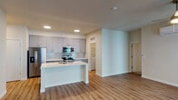 Located at 3158 SW 12th Ave in Portland, Oregon, this single-floor residence offers a thoughtfully designed open-concept layout with modern finishes throughout. The living area is bright and welcoming, featuring warm-toned hardwood-style flooring, a ceiling fan with integrated lighting, and a glass door that opens to a private balcony, allowing natural light to fill the space. A wall-mounted mini-split system provides efficient climate control.

The kitchen is a standout feature, equipped with sleek gray cabinetry, a subway tile backsplash, white quartz countertops, and a full suite of stainless steel appliances including a refrigerator with ice dispenser, electric range, and microwave. A center island with a sink offers additional prep space and a natural gathering point.

Adjacent to the kitchen, a dedicated laundry closet houses a stacked washer and dryer for added convenience. The bedroom includes plush carpeting and a generously sized sliding-door closet with built-in shelving. Two full bathrooms are finished with white quartz vanities, undermount sinks, modern fixtures, and large mirrors. One bathroom features a tub-shower combination, while the other offers a walk-in shower. The overall design is clean, contemporary, and highly functional.
