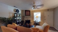 This single-floor residence offers a well-organized layout with distinct living, dining, and kitchen areas that flow cohesively together. The living room serves as the heart of the home, anchored by a corner brick fireplace that adds warmth and character to the space. A ceiling fan with integrated lighting hangs overhead, complementing the textured ceiling throughout. Natural light filters in through a window fitted with blinds, while a decorative open shelving unit provides both storage and display space. Framed wall art adds visual interest and a touch of personality to the room.

The dining area connects seamlessly to the living room, featuring hardwood-style flooring, a glass-top dining table with dark chairs, and additional wall art that continues the warm, earthy aesthetic of the home. A pendant light above the dining space enhances the intimate atmosphere.

The kitchen is efficiently designed with white cabinetry offering generous storage, dark speckled countertops, a double stainless steel sink, and black appliances including a refrigerator. The layout maximizes functionality within a compact footprint, making it practical for everyday use. Overall, the space presents a warm, inviting ambiance with consistent design elements throughout.