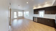 This single-floor 2-bedroom, 2-bathroom residence offers a clean, contemporary design throughout. The open-concept living and dining area is anchored by light hardwood-style flooring and multiple windows fitted with blinds, allowing generous natural light to fill the space. Views of nearby palm trees add a pleasant outdoor element to the living area, which also features access to an exterior door.

The kitchen is well-equipped with dark espresso-toned cabinetry, white quartz-style countertops, and a full suite of stainless steel appliances including a refrigerator, range with oven, over-the-range microwave, and dishwasher. The hardwood-style flooring continues seamlessly from the kitchen into the living space, creating a cohesive aesthetic.

Both bedrooms are carpeted and feature neutral white walls, individual windows with blinds offering outdoor views, and ample wall space for flexible furniture arrangement. Each room maintains a calm, functional atmosphere.

The two bathrooms mirror each other in design, each featuring dark wood vanities with white countertops, built-in open shelving, large mirrors with overhead lighting, hardwood-style tile flooring, and a tub-shower combination. The overall aesthetic of the unit is modern and consistent, with a neutral palette that provides a versatile and inviting living environment.