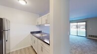 This single-story residence offers a practical and well-organized layout with clearly defined living spaces. The kitchen is a standout feature, designed in a galley style with white cabinetry fitted with brushed nickel hardware, dark countertops, and light wood-look vinyl flooring. Stainless steel appliances—including a refrigerator, electric range, and over-the-range microwave—provide a modern, cohesive look. A single-basin sink with under-cabinet lighting adds functionality to the workspace. The kitchen opens toward the main living area via a half-wall partition, promoting a connected feel between spaces.

The living area is generously proportioned, finished with neutral-toned carpet and a ceiling fan overhead. A large sliding glass door fitted with vertical blinds allows natural light to fill the room and provides outdoor access. Adjacent to the living space, a hallway connects to additional rooms, with multiple closet doors visible along the corridor.

The bedrooms are carpeted and finished in soft neutral tones, each receiving natural light through windows dressed with vertical blinds. One bedroom features a spacious walk-in closet with a distinctive accent-colored interior. The overall aesthetic throughout is clean, minimal, and move-in ready, with consistent neutral finishes across all spaces.