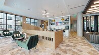 Located at 525 E 21st St in Charlotte's vibrant Plaza Midwood neighborhood, this single-floor amenity space blends contemporary design with inviting, functional zones throughout. The signature hexagonal tile flooring flows seamlessly across the entire space, unifying distinct areas under a cohesive aesthetic.

The main lounge area features exposed brick walls, floor-to-ceiling grid-pane windows that flood the space with natural light and offer direct views of the landscaped courtyard. Plush green accent chairs and leather seating are arranged around a sculptural wood slatted divider, creating a relaxed yet refined atmosphere.

A full bar-style counter with bar seating, warm wood cabinetry, open black metal shelving, and gold pendant lighting serves as a central social hub, complemented by a sink, beverage station, and flat-screen display. Adjacent dining areas offer navy blue booth seating and a live-edge communal table beneath globe pendants and decorative exposed pipe detailing on brick walls.

Private work nooks lined in amber upholstery provide semi-enclosed spaces ideal for focused work or quiet conversations. A glass-enclosed conference or meeting room adds a professional touch, while bold wall murals and curated artwork lend an artistic character throughout. The overall ambiance is modern, energetic, and thoughtfully designed for both productivity and community gathering.