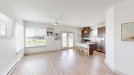 This single-story, 3-bedroom, 2-bathroom home offers a thoughtfully designed open-concept layout that maximizes both functionality and comfort. The combined kitchen and living area serves as the heart of the home, featuring light wood-style flooring, large windows, and a ceiling fan that fill the space with natural light and a bright, airy ambiance. French doors provide additional access to the outdoors, further enhancing the open feel.

The kitchen is well-equipped with rich dark-toned cabinetry, stainless steel appliances, a tile backsplash, and a central island with a granite-style countertop and seating for multiple bar stools. Pendant lighting above the island adds a modern touch. The living area is generously sized, with corner windows that invite ample daylight and views of the surrounding neighborhood.

The bedrooms are carpeted and feature windows with blinds, ceiling fans, and baseboard heating. The primary bedroom includes a walk-in closet outfitted with wrap-around wire shelving for versatile storage. The bathrooms are finished with granite-topped vanities, dark-framed mirrors, and wood-style flooring.

A dedicated laundry room houses a full-size washer and dryer with additional wire shelving overhead. The home's clean, neutral palette and consistent finishes create a cohesive and inviting atmosphere throughout.