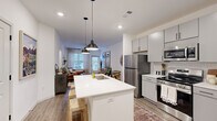 Located at 6773 Campus Dr in Colorado Springs, CO, this well-designed one-bedroom, one-bathroom residence offers a thoughtful single-story layout with modern finishes throughout. The open-concept living and kitchen area forms the heart of the home, anchored by a white quartz kitchen island with bar seating and pendant lighting overhead. The kitchen is equipped with stainless steel appliances, gray shaker-style cabinetry with matte black hardware, and a herringbone tile backsplash, all set atop wood-look flooring that extends into the living area. The living room receives natural light through large windows and a glass door, with a ceiling fan adding comfort. The bedroom features plush carpeting, a ceiling fan, and a generous window that fills the room with natural light. A spacious walk-in closet with built-in shelving and hanging rods provides ample storage. The full bathroom impresses with a dual-sink vanity, gray cabinetry, framed mirrors, wood-look flooring, and a tub-shower combination with marble-style tile surround. Direct access from the bathroom to the walk-in closet enhances everyday functionality. The overall aesthetic is clean, contemporary, and cohesive throughout.