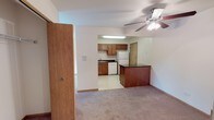 This single-floor unit offers a functional and well-organized layout designed for comfortable everyday living. The living area is generously sized, finished with plush wall-to-wall carpeting and neutral white walls that create a clean, versatile backdrop. A ceiling fan with integrated lighting anchors the space, and a sliding glass door opens directly onto a private balcony overlooking a lush, green outdoor setting, filling the room with natural light.

The kitchen is open to the living area and separated by a raised peninsula counter finished with a dark laminate surface, providing additional prep and seating space. The kitchen itself features warm oak cabinetry extending to the ceiling for ample storage, dark countertops, a double stainless steel sink, and white appliances including a refrigerator, dishwasher, and range. The floor is finished in classic white tile.

The bedrooms are carpeted and bright, each with windows that bring in natural light and views of the surrounding greenery. One bedroom includes a built-in cabinet unit beneath the window. A full bathroom serves the unit, complete with a tiled tub-shower combination, white fixtures, a wood-toned vanity, and tile flooring. A large closet provides additional storage within the living space.