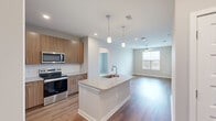 Located at 501 W Waugh St in Dalton, GA, this well-designed 2-bedroom, 2-bathroom residence offers a thoughtful single-floor layout with modern finishes throughout. The open-concept kitchen and living area serves as the heart of the home, featuring a central island with a granite countertop and undermount sink, illuminated by stylish pendant lighting. The kitchen is equipped with stainless steel appliances, including a range, microwave, and refrigerator, complemented by warm wood-toned cabinetry and a classic white subway tile backsplash. Durable hardwood-style flooring flows through the main living areas, while the living room benefits from natural light through large windows and a ceiling fan overhead. Both bedrooms are carpeted for comfort, with the secondary bedroom featuring a window with outdoor views. The bathrooms are finished with granite-topped vanities, wood-toned cabinetry, and subway tile surrounds on the tub-shower combinations. Each bedroom is served by a dedicated closet with built-in wire shelving systems, offering generous storage. The neutral color palette and clean architectural lines throughout give the space a bright, contemporary feel.