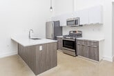 Located at 1209 Morse Ave in Royal Oak, Michigan, this single-floor space showcases a modern, minimalist aesthetic throughout. The open-concept kitchen is a standout feature, boasting soaring ceilings that amplify the sense of space and airiness. It is equipped with a full suite of stainless steel appliances, including a gas range, microwave, and refrigerator, complemented by two-tone cabinetry — sleek white upper cabinets paired with wood-finish lower cabinets — and bright white countertops. A peninsula with an integrated sink and pendant lighting adds both function and style to the kitchen area. The living area continues the clean, open feel with neutral-toned concrete-style flooring and crisp white walls. Storage is well-addressed with two walk-in closets: one features built-in shelving, hanging rods, and dedicated shoe storage, while the second offers a simpler layout with a full-width hanging rod. The bathrooms are thoughtfully designed; one features a frameless glass walk-in shower with tile surround and mosaic tile flooring, while the second includes a soaking tub and tiled shower surround with a floating vanity and large-format tile flooring. The overall design is clean, contemporary, and move-in ready.