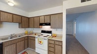 Located at 3301 Wible Rd in Bakersfield, California, this single-story unit offers a practical and comfortable layout designed for everyday living. The kitchen is fitted with an L-shaped arrangement of warm wood-toned cabinetry that provides generous storage, light-colored countertops, a white electric coil range with an overhead exhaust hood, a double sink, and a dishwasher. The tile flooring in the kitchen transitions into carpeted living spaces throughout the rest of the unit. The spacious living area features neutral walls, a textured ceiling, and vertical blinds over a large sliding glass door that allows natural light to fill the room. The bedrooms are carpeted and well-proportioned, each with windows dressed in vertical blinds that provide privacy while welcoming daylight. The bathroom includes a tub and shower combination enclosed by sliding glass doors, a vanity with wood cabinetry and a mirrored medicine cabinet, and tile flooring. A secondary vanity area is accessible from a hallway, offering additional counter space and storage. The overall aesthetic is clean, neutral, and functional, providing a comfortable living environment in a convenient Bakersfield location.