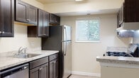 This single-floor unit offers a well-designed, functional layout that maximizes comfort and usability throughout. The open-concept living and dining area flows seamlessly into the kitchen, which is defined by a peninsula breakfast bar that provides both additional counter space and a natural visual divider. The kitchen is well-appointed with rich dark cabinetry, light granite-style countertops, and a full suite of stainless steel appliances including a refrigerator, gas range, and dishwasher. A window above the sink invites natural light and outdoor greenery views into the kitchen space.

The living area is bright and airy, with warm beige walls, light wood-style flooring that extends throughout the unit, and a large window fitted with white blinds that frames views of surrounding trees. The bedrooms continue the same cohesive aesthetic, each featuring the same durable wood-style flooring, soft neutral wall tones, and generous windows that allow natural light to fill the rooms. Closet access is also present in the bedroom areas.

The bathroom is clean and straightforward, featuring a tub-shower combination with white surround panels and standard fixtures. A separate water closet area provides added privacy. Throughout the unit, the consistent color palette and modern finishes create a cohesive, move-in-ready environment.