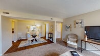 Located at 409 Tradewinds Dr in Fayetteville, NC, this single-story residence offers a well-organized and functional floor plan designed for comfortable everyday living. The open living and dining area serves as the heart of the home, where warm-toned carpet flows through the living room while rich hardwood flooring defines the dining space. The dining area accommodates a round glass table with elegant chairs, complemented by soft overhead lighting. The living room features large windows that invite natural light and provide a bright, welcoming atmosphere. The kitchen is outfitted with white cabinetry, ample storage, and full appliances including a refrigerator, electric range, and built-in microwave. The primary bedroom is generously sized, featuring plush carpet, a ceiling fan with light fixture, and direct access to a private bathroom complete with a tub-shower combination. A second bedroom offers flexibility, with room for multiple beds, its own ceiling fan, and a walk-in closet. A shared full bathroom with tiled flooring and a tub-shower unit serves additional occupants. Textured ceilings and neutral wall tones carry throughout, creating a cohesive and understated aesthetic across all rooms.