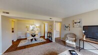 Located at 409 Tradewinds Dr in Fayetteville, NC, this single-story residence offers a well-organized and functional floor plan designed for comfortable everyday living. The open living and dining area serves as the heart of the home, where warm-toned carpet flows through the living room while rich hardwood flooring defines the dining space. The dining area accommodates a round glass table with elegant chairs, complemented by soft overhead lighting. The living room features large windows that invite natural light and provide a bright, welcoming atmosphere. The kitchen is outfitted with white cabinetry, ample storage, and full appliances including a refrigerator, electric range, and built-in microwave. The primary bedroom is generously sized, featuring plush carpet, a ceiling fan with light fixture, and direct access to a private bathroom complete with a tub-shower combination. A second bedroom offers flexibility, with room for multiple beds, its own ceiling fan, and a walk-in closet. A shared full bathroom with tiled flooring and a tub-shower unit serves additional occupants. Textured ceilings and neutral wall tones carry throughout, creating a cohesive and understated aesthetic across all rooms.
