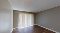 Located at 11355 Zapata in San Diego, Unit #20 is a thoughtfully designed single-floor residence that offers a clean, functional layout with consistent neutral tones and quality finishes throughout. The living area is spacious and inviting, featuring rich dark hardwood-style flooring, textured ceilings, and a large sliding glass door dressed with vertical blinds that fills the room with abundant natural light. The open flow of the living space connects seamlessly to the kitchen and additional areas, making the layout feel cohesive and easy to navigate. The kitchen is well-equipped, showcasing crisp white shaker-style cabinetry, gray countertops, stainless steel appliances including a refrigerator and range, and light hardwood-style flooring that brightens the space. The bedroom offers a comfortable, serene environment with plush carpeting, a window with vertical blinds allowing natural light, and a closet with sliding mirror doors. The bathroom is practical and neatly finished, featuring a full shower-tub combination, a vanity with gray countertops, and hardwood-style flooring. Throughout the residence, white baseboards and neutral warm-gray walls provide a clean, move-in-ready aesthetic that suits a variety of furnishing styles.