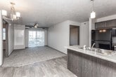 This single-floor unit is designed with an open-concept layout that connects the kitchen and living area, creating a cohesive and functional main living space. The kitchen features dark cabinetry with brushed nickel hardware, laminate countertops, a peninsula with an undermount sink and pendant lighting above, and black appliances including a refrigerator and range. The flooring transitions from wood-look planking in the kitchen and entry areas to plush carpet throughout the living room and bedrooms, providing a comfortable contrast of textures.

The living area is generously sized and benefits from a ceiling fan and a sliding glass door that opens to a private balcony, allowing natural light to fill the space. A wall-mounted heating and cooling unit ensures year-round comfort. A chandelier fixture adds ambient illumination near the entryway.

Two bedrooms are carpeted and each features a window with blinds, offering views of the surrounding area. Both bathrooms are finished with large-format tile flooring, dark vanity cabinetry with white countertops, and a full tub-shower combination with chrome fixtures. An in-unit laundry closet provides added convenience. The overall aesthetic is clean and functional, with a consistent dark-trim and neutral-wall palette throughout.
