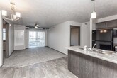 This single-floor unit is designed with an open-concept layout that connects the kitchen and living area, creating a cohesive and functional main living space. The kitchen features dark cabinetry with brushed nickel hardware, laminate countertops, a peninsula with an undermount sink and pendant lighting above, and black appliances including a refrigerator and range. The flooring transitions from wood-look planking in the kitchen and entry areas to plush carpet throughout the living room and bedrooms, providing a comfortable contrast of textures.

The living area is generously sized and benefits from a ceiling fan and a sliding glass door that opens to a private balcony, allowing natural light to fill the space. A wall-mounted heating and cooling unit ensures year-round comfort. A chandelier fixture adds ambient illumination near the entryway.

Two bedrooms are carpeted and each features a window with blinds, offering views of the surrounding area. Both bathrooms are finished with large-format tile flooring, dark vanity cabinetry with white countertops, and a full tub-shower combination with chrome fixtures. An in-unit laundry closet provides added convenience. The overall aesthetic is clean and functional, with a consistent dark-trim and neutral-wall palette throughout.