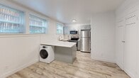 Located at 435 E 100 S in Salt Lake City, Utah, this thoughtfully designed studio unit makes efficient use of its compact footprint across a single floor. The open-plan living, dining, and kitchen area serves as the heart of the space, anchored by a central island with a crisp white countertop that doubles as a prep and dining surface. The kitchen is outfitted with stainless steel appliances — including a full-size refrigerator, electric range, and over-the-range microwave — complemented by soft gray shaker-style cabinetry and a classic white subway tile backsplash. A stainless steel sink sits beneath dual windows that invite natural light. An in-unit front-load washer is neatly integrated into the kitchen island base, adding everyday convenience. Light wood-look plank flooring runs throughout the living area, enhancing the bright, airy atmosphere. A wall-mounted mini-split heating and cooling unit ensures year-round comfort, and an electrical panel is discreetly housed on the living room wall. The bathroom features a full soaking tub and shower combo surrounded by floor-to-ceiling white subway tile, a pedestal sink, and a round mirror. Two closets provide practical storage within this well-appointed, move-in-ready studio.
