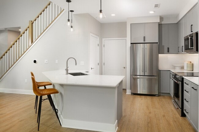 Signature Collection kitchen with stainless steel appliances, white quartz countertop, grey cabinetry, white quartz backsplash, hard surface flooring, and pendant lighting - Avalon Wayne