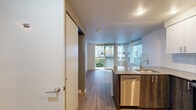 Located at 766 Garfield St, Unit 306 in Seattle's Queen Anne neighborhood, this two-bedroom, one-bathroom residence offers a thoughtfully designed layout across a single floor. The kitchen is a standout feature, outfitted with stainless steel appliances including a refrigerator, range, and microwave, complemented by white cabinetry, a tile backsplash, and a peninsula with dark countertops — ideal for both cooking and casual dining. Hardwood-style flooring runs throughout the main living areas, adding warmth and continuity to the open-concept space. The living area is bathed in natural light through large sliding glass doors that open onto a private balcony, offering views of the surrounding urban greenery and neighboring buildings. The primary bedroom features carpeted flooring and a window with outdoor views, while the second bedroom also benefits from ample natural light. The bathroom is cleanly finished with tile accents, a combination tub and shower, and white cabinetry. A second kitchen area provides additional functionality. The unit's light-toned walls and modern finishes throughout create a clean, contemporary ambiance well-suited to urban living in Seattle.