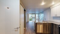 Located at 766 Garfield St, Unit 306 in Seattle's Queen Anne neighborhood, this two-bedroom, one-bathroom residence offers a thoughtfully designed layout across a single floor. The kitchen is a standout feature, outfitted with stainless steel appliances including a refrigerator, range, and microwave, complemented by white cabinetry, a tile backsplash, and a peninsula with dark countertops — ideal for both cooking and casual dining. Hardwood-style flooring runs throughout the main living areas, adding warmth and continuity to the open-concept space. The living area is bathed in natural light through large sliding glass doors that open onto a private balcony, offering views of the surrounding urban greenery and neighboring buildings. The primary bedroom features carpeted flooring and a window with outdoor views, while the second bedroom also benefits from ample natural light. The bathroom is cleanly finished with tile accents, a combination tub and shower, and white cabinetry. A second kitchen area provides additional functionality. The unit's light-toned walls and modern finishes throughout create a clean, contemporary ambiance well-suited to urban living in Seattle.