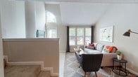 This two-story home at 499 Northside Cir in Atlanta, Georgia offers a thoughtfully designed layout spread across two levels. The living room is a standout space, boasting soaring vaulted ceilings with an arched clerestory window that floods the room with natural light. Large front-facing windows with classic blinds and draping curtains frame views of the lush surroundings. A fireplace anchors the living area, adding warmth and character to the open atmosphere. Soft carpeting and neutral tones throughout create a calm, welcoming ambiance. The kitchen features rich dark cabinetry, granite-style countertops, hardwood-style flooring, and black appliances, offering both style and functionality in a well-organized galley layout. Upstairs, the spacious bedroom is bathed in natural light through a generous window dressed with bold accent curtains. The room includes a walk-in closet and direct access to a full bathroom complete with a shower-tub combo. A hallway leading to the living area is accented with framed artwork, adding a personal touch. The staircase connects both levels seamlessly, with an open railing that enhances the airy, open feel of the home throughout.
