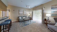 Located at 303 Mill Pond Ln in Salisbury, Maryland, this single-floor residence offers a well-organized layout designed for comfortable everyday living. The kitchen is appointed with warm honey-toned wood cabinetry, dark countertops, a double-basin sink, and white appliances including a refrigerator and range, all set above light hardwood-style flooring that adds a clean, bright feel to the space. Adjacent to the kitchen, the living area is carpeted and generously sized, featuring track lighting and a sliding glass door that fills the room with natural light and provides views of the surrounding greenery. A separate seating nook connects seamlessly to the main living space, offering additional flexibility for lounging or entertaining. The residence includes two carpeted bedrooms, each with neutral-toned walls and ample natural light from large windows. Both rooms are well-proportioned, with the primary bedroom featuring a ceiling fan and space for a full bedroom suite. The bathroom is finished with white tile surrounding the tub-shower combination, wood-style flooring, and a vanity with under-sink storage. Throughout the residence, a consistent palette of warm beige and sage tones creates a cohesive and inviting atmosphere.