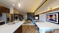 Located at 37 Half Day Rd in Lincolnshire, IL, this single-floor residence blends modern design with industrial-chic character. The open-concept layout connects the kitchen and living areas seamlessly, creating a spacious, flowing environment throughout.

The kitchen is outfitted with dark espresso cabinetry reaching toward the ceiling, stainless steel appliances including a gas range, microwave, and French door refrigerator, complemented by a large central island with a white quartz countertop and an integrated sink. A glass tile backsplash and pendant lighting add refined touches, while sliding glass doors invite natural light and outdoor access.

The living area is a standout, anchored by a striking geometric laser-cut decorative wall panel that serves as a bold focal point. Exposed metal ductwork runs along the upper wall, adding an industrial edge, while warm LED strip lighting beneath a wood-paneled valance creates an inviting ambiance. White-painted brick along one wall adds texture and warmth. Rich hardwood flooring flows throughout the main living space.

A dedicated workspace area is thoughtfully integrated into the layout, offering functional versatility. The bathroom features large-format light tile flooring, a generous double-sink vanity with dark cabinetry and quartz countertops, and a clean, minimalist aesthetic. Overall, the space delivers a sophisticated urban living experience with curated design details at every turn.