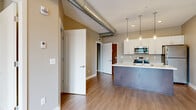 Located at 655 Goodman St S in Rochester, NY, this well-designed one-bedroom, one-bathroom unit offers a thoughtfully laid-out single-floor plan with modern finishes throughout. The open-concept kitchen and living area serves as the heart of the space, featuring a striking peninsula with a concrete-style base and light quartz countertop, white shaker cabinetry, stainless steel appliances including a range, microwave, and refrigerator, and stylish cylindrical pendant lights overhead. Exposed ductwork adds an industrial-chic character to the space. Light wood-tone flooring flows continuously throughout, tying together each room with a cohesive, contemporary aesthetic. The living area benefits from access to a private exterior door, flanked by windows that invite an abundance of natural light and provide views of the surrounding neighborhood. The generously sized bedroom features a large window with city views, recessed lighting, and the same warm flooring. The bathroom is finished with large-format tile flooring, a dark-cabinetry vanity with a white countertop, a glass-enclosed walk-in shower, and clean, neutral wall tones. Two hallways connect the spaces efficiently, contributing to the unit's smart and functional layout.