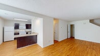 This two-story residence offers a well-organized layout across both levels, combining functional design with comfortable living spaces throughout. The main level features warm-toned hardwood flooring that runs continuously through the open living and dining areas, creating a bright and cohesive feel. Large windows allow natural light to fill the space, while a staircase connects to the upper floor. The kitchen is thoughtfully designed with rich dark-wood cabinetry, granite-style countertops, a breakfast bar peninsula, and a full suite of white appliances including a refrigerator, range, microwave, and dishwasher. A pass-through opening connects the kitchen to the main living area, enhancing the open-concept flow. The upper level houses multiple bedrooms, each finished with plush neutral carpeting and generously sized windows that frame outdoor greenery. The bedrooms offer ample space and a calm, airy atmosphere. Two full bathrooms are present in the home, each featuring a tub-shower combination, a vanity with granite-style countertops, dark wood cabinetry, and hardwood flooring. Textured ceilings are found throughout, and the overall interior palette of crisp whites and warm neutrals gives the home a clean, inviting character.