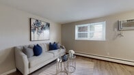 This single-floor residence offers a thoughtfully designed layout that balances comfort and functionality. The living room serves as a welcoming focal point, featuring warm hardwood-style flooring, neutral beige walls, and a bright window with slatted blinds that allows natural light to fill the space. A baseboard heating system runs along the perimeter, and the room provides ample space for relaxed seating arrangements.

The kitchen is well-equipped and stylish, showcasing white shaker-style cabinetry, granite-look countertops, and a classic subway tile backsplash. Stainless steel appliances—including a gas range, over-the-range microwave, and refrigerator—lend a modern, polished feel. A pass-through window connects the kitchen to an adjoining area, enhancing the open flow of the space.

The bedroom is a serene retreat with soft carpeting, neutral tones, and a window that brings in natural light. A set of full-width bifold closet doors provides generous storage capacity, keeping the room organized and uncluttered.

The bathroom is clean and straightforward, featuring tile flooring, a full soaking tub with a shower, and crisp white fixtures throughout. The overall ambiance of this residence is calm and inviting, with a cohesive neutral palette that makes each room feel bright and move-in ready.