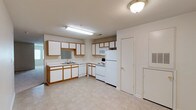 This single-floor, 3-bedroom, 2-bathroom home offers a practical and comfortable layout designed to maximize livability. The kitchen features an L-shaped configuration with white cabinetry accented by wood-tone trim, providing ample storage across both upper and lower cabinets. It is equipped with a full suite of white appliances, including a refrigerator, electric range, microwave, and dishwasher, set atop neutral tile flooring that extends throughout the kitchen area. A pass-through window connects the kitchen to the adjacent living space, promoting an open feel between the two areas. The living and dining areas are carpeted in a neutral tone, offering a seamless and open flow ideal for everyday use. Natural light filters through windows in the living space and bedrooms, creating a bright and welcoming atmosphere throughout. Each of the three bedrooms is finished with plush carpet and neutral wall tones, providing a clean and versatile canvas. Select bedrooms include ceiling fans and windows with blinds for added comfort and privacy. The two bathrooms are finished with tile flooring and feature tub-shower combinations with clean white surrounds, vanities with wood-accented cabinetry, and mirrors. A washer and dryer area is also present within the unit, adding functional convenience.