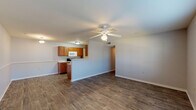 This single-floor residence offers a practical and well-organized layout designed to maximize functionality. The open-concept living area is highlighted by durable wood-style flooring, neutral gray walls, and a ceiling fan with integrated lighting. A chair rail detail runs along the dining area wall, adding a subtle architectural touch. Large windows allow natural light to fill the space, creating a bright and welcoming atmosphere.

The kitchen is laid out in a galley configuration, featuring warm medium-toned wood cabinetry, light countertops, and white appliances including a range, over-the-range microwave, refrigerator, and dishwasher. A peninsula counter separates the kitchen from the living area, providing additional prep space and an open sightline. A utility panel is accessible from within the kitchen corridor.

The bedrooms are carpeted for comfort and each include a ceiling fan with a light fixture. Windows bring in natural light and views of the outdoors, contributing to an airy feel in each room. The bathrooms are functional and clean, each equipped with a full tub and shower combination featuring chrome fixtures and white surrounds, with cabinetry providing convenient overhead storage.