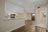 This single-story residence offers a well-organized layout with a neutral palette and clean finishes throughout. The open living area is anchored by warm wood-style flooring and flows directly toward a sliding glass door that leads to a private balcony, filling the space with natural light and offering pleasant outdoor views of surrounding greenery. A half-wall partition separates the living area from the galley-style kitchen, which features white cabinetry, light stone-look countertops, a double-basin sink, and a full suite of stainless steel appliances including a refrigerator, range, microwave, and dishwasher. The layout maximizes efficiency while maintaining an open feel. The bedrooms are carpeted for comfort and each includes a ceiling fan with a generously sized window that frames outdoor views and invites natural light. The textured ceilings are consistent throughout the unit, adding subtle dimension. The bathroom is finished in crisp white tones, featuring a combined tub and shower surround, a white vanity with a marble-look countertop, a large mirror, and wood-style flooring that ties back to the main living areas. Overall, the space presents a bright, functional, and cohesive design.